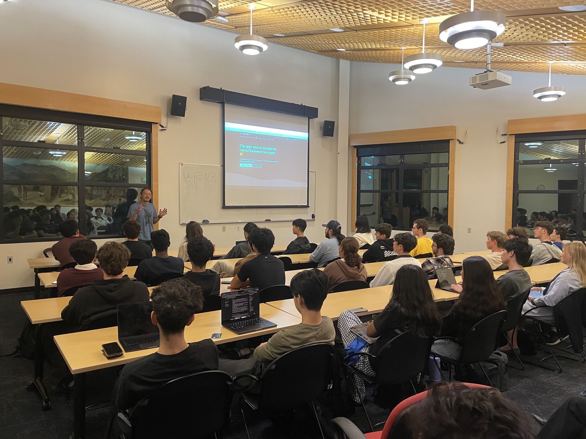 Michael Feng speaking to a seated audience beside a projected Hummingbot slide